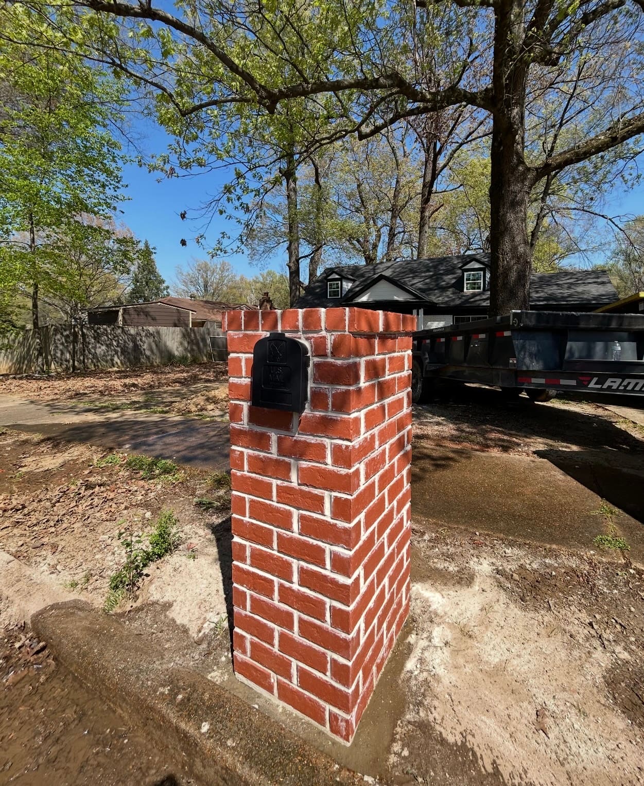 Red brick mailbox column with a capped top, set at the edge of a driveway